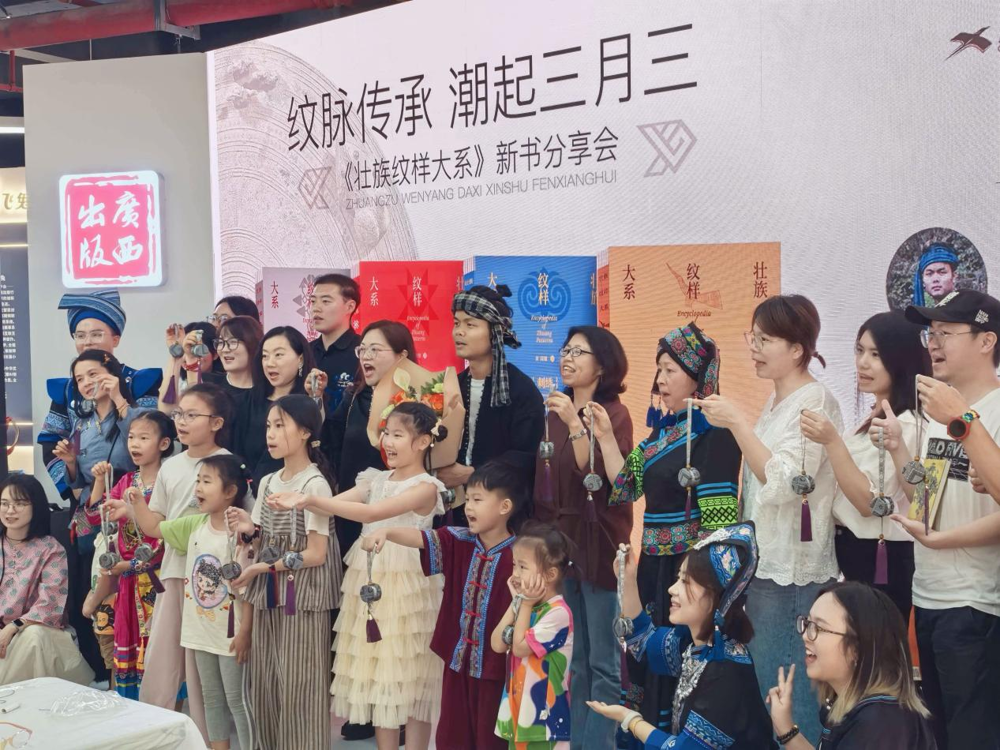 现场嘉宾与观众带着亲手制作的壮锦铜鼓挂饰合影留念
